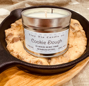 A 'Cookie Dough' homemade soy candle by Tiny Tin Candle Co. is nestled in a cast-iron skillet beside freshly baked cookies, evoking the irresistible scent of home baking