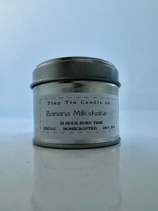 Tiny Tin Candle Co.'s homemade candle 'Banana Milkshake' soy candle, lit to infuse any room with its sweet, inviting fragrance. front of candle with lid on 