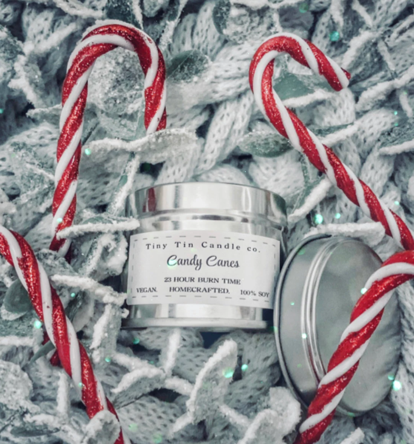 Tiny Tin Candle Co.'s Candy Canes homemade candle in a silver tin, surrounded by red and white candy canes on a white knitted background, highlighting its artisanal charm and festive theme