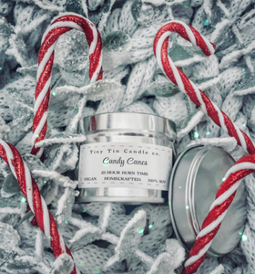 Tiny Tin Candle Co.'s Candy Canes homemade candle in a silver tin, surrounded by red and white candy canes on a white knitted background, highlighting its artisanal charm and festive theme