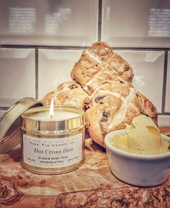 Indulge in the essence of Easter with Tiny Tin Candle Co.'s 'Hot Cross Bun' candle, displayed alongside freshly baked buns and creamy butter, capturing the homemade candle spirit of the holiday