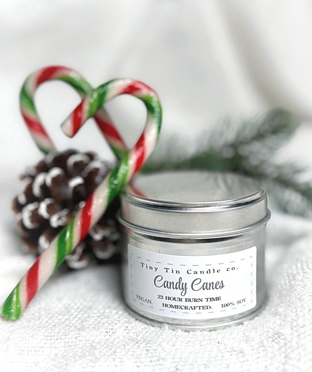 Tiny Tin Candle Co.'s Candy Canes homemade candle in a silver tin, surrounded by red and white candy canes on a white knitted background, highlighting its artisanal charm and festive theme